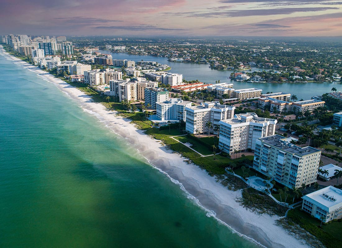 Naples, FL - Aerial View of Commercial Buildings and Apartments on the Beach Against a Colorful Sunset Sky in Naples Florida